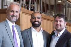 A professor and two business students, all in suits, standing shoulder to shoulder.